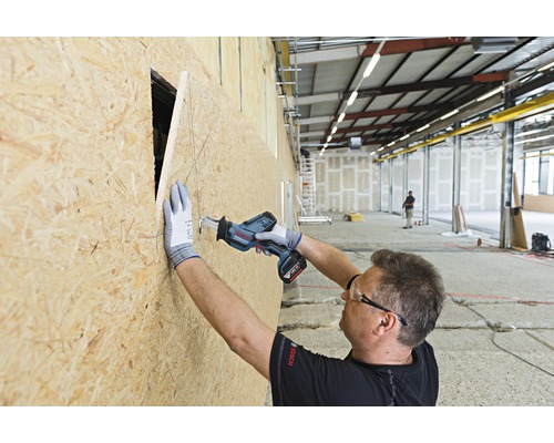 Řemeslník řeže otvor do dřevěné desky pomocí akumulátorové ocasky.