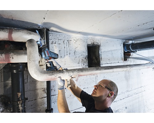 Muž řeže potrubí v suterénu pomocí akumulátorové ocasky.