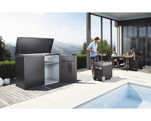 Zahradní scéna s domkem na nářadí, grilem a rodinou u jídelního stolu na terase