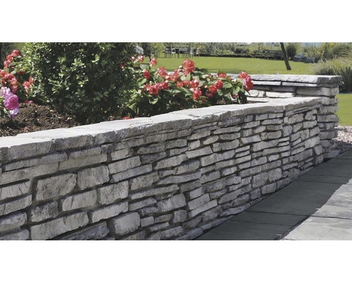 Stohovaná kamenná zeď v zahradě s rostlinami