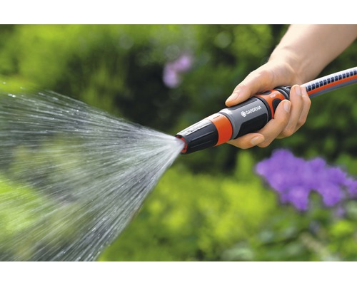 Osoba drží zahradní hadici s rozstřikovací tryskou, ze které vytéká voda.