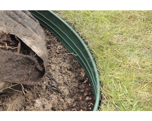 Detailní záběr na zelený plastový okraj trávníku, který ohraničuje zahradní plochu.