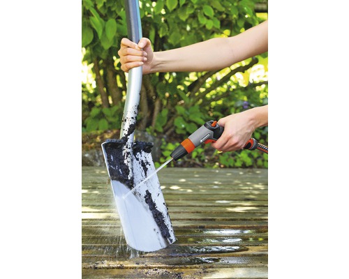 Osoba čistí lopatu proudem vody na dřevěném povrchu.