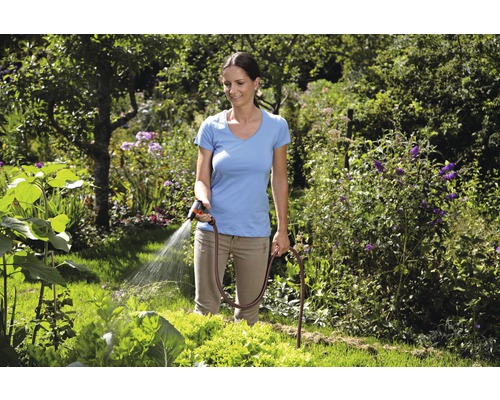 Žena zalévá zahradu zahradní hadicí a stříkací pistolí