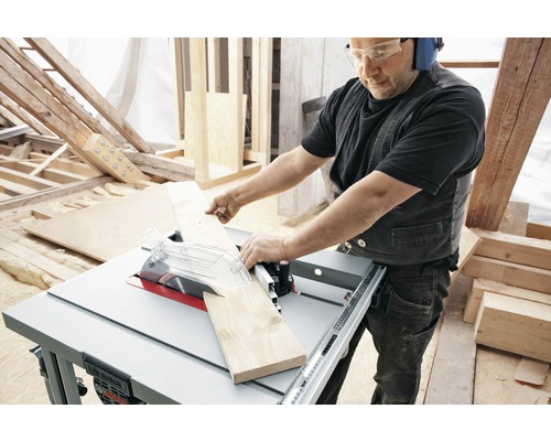 Muž řeže dřevěnou desku stolní pilou ve světlé dílně