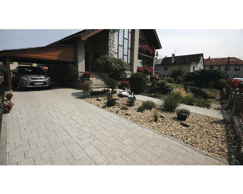 Příjezdová cesta s dlažebními kostkami, přístřešek pro auto a dům s kamennou fasádou