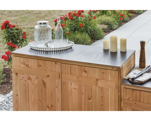 Zahradní bar s dřevěným obkladem, dávkovač nápojů, láhev, sklenice, svíčky a grilovací kleště na horní straně