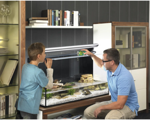 Akvárium se dvěma želvami, muž a dítě krmí zvířata v jasném obytném prostředí.