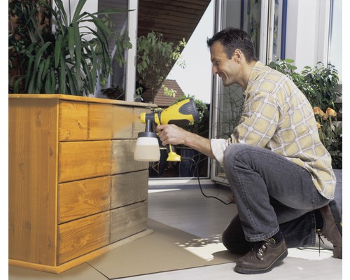 Muž stříká barvou dřevěnou komodu pomocí stříkací pistole.