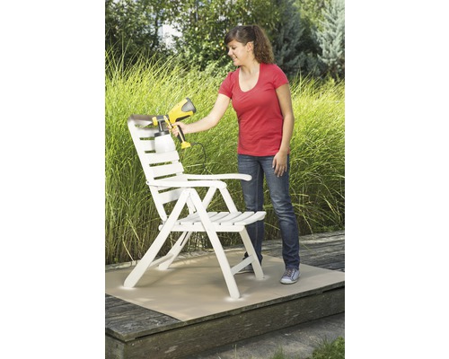 Žena natírá dřevěnou židli stříkací pistolí na barvy na zahradě.