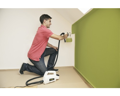 Muž natírá stěnu pomocí stříkacího systému na barvy