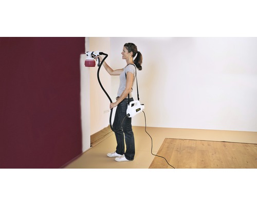 Žena maluje stěnu barvicím stříkacím systémem v místnosti