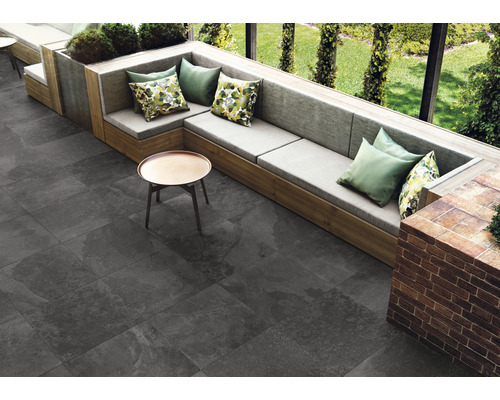 Venkovní prostor s šedou dlažbou, posezení s polštáři a malým stolem