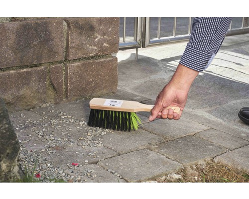 Osoba používá smeták s dřevěnou rukojetí k čištění dlažebních kostek.