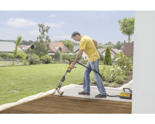 Muž ošetřuje dřevěnou terasu pomocí stříkacího systému Wagner na zahradě.