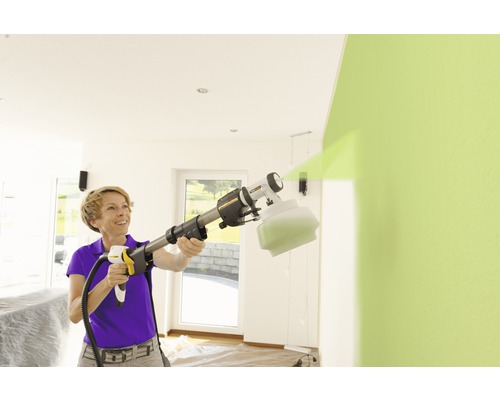 Žena používá systém stříkání barev k natírání zdi v interiéru.