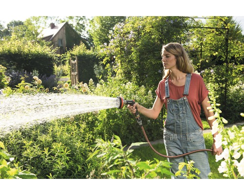 Žena zalévá zahradu zahradní hadicí a postřikovačem