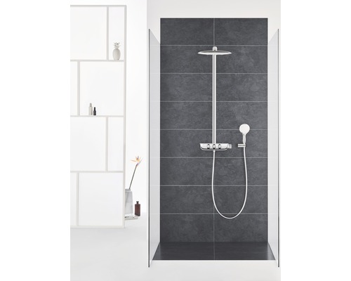 Sprchový systém s hlavovou a ruční sprchou v koupelně s tmavými dlaždicemi.