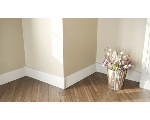 Stěnový spoj s bílými podlahovými lištami, květinová vazba na dřevěné podlaze