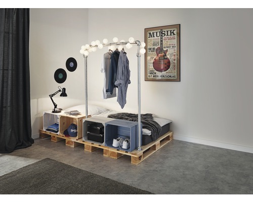 Ložnice s postelí z dřevěných palet, zdobená světelným řetězem a hudebním plakátem