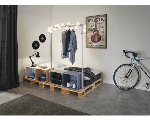 Ložnice s paletovou postelí, věšák na šaty s osvětlením a ozdobné bedny