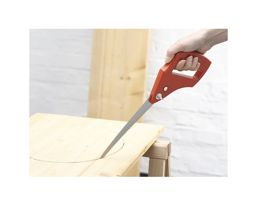 Přímočará pila s červenou rukojetí vyřezává otvor do dřevěné desky.
