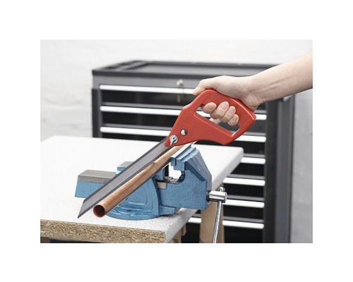 Ruční pila řeže trubku upevněnou ve svěráku