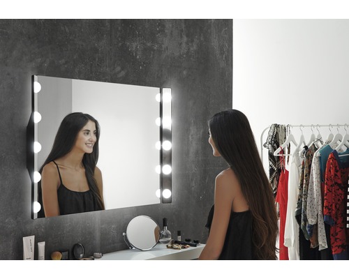 Žena před osvětleným kosmetickým zrcadlem v koupelně.