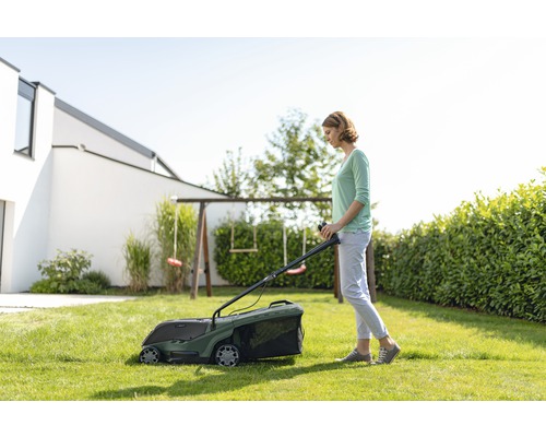Žena seče trávník sekačkou na trávu na zahradě.