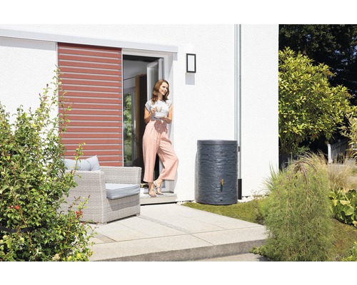 Nádrž na dešťovou vodu v zahradě vedle ženy a domu