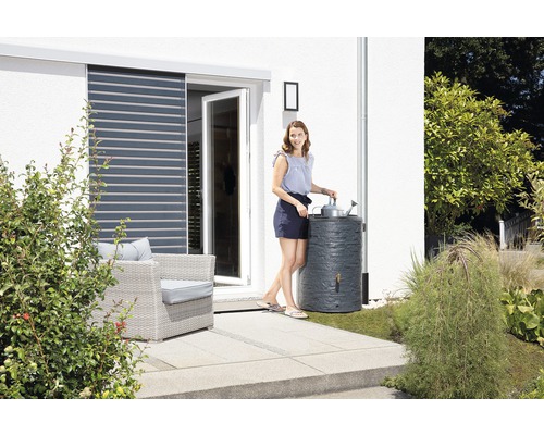 Žena zalévá rostliny dešťovou vodou z nádrže na dešťovou vodu v zahradě.