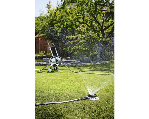 Zahradní scéna se zavlažovačem trávníku a hadicovým vozíkem pro zavlažování