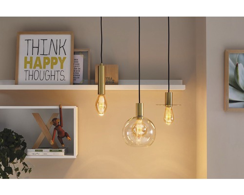 Tři závěsná svítidla různých tvarů se zlatými prvky před policemi