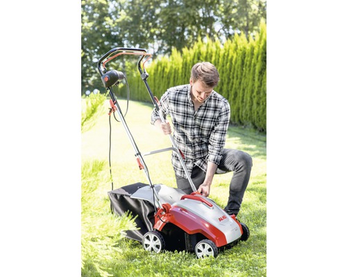 Muž obsluhuje provzdušňovač trávníku na zahradě. Přístroj má sběrný koš.