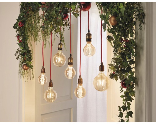 Ozdobné žárovky visí z girlandy s rostlinami a vánočními koulemi