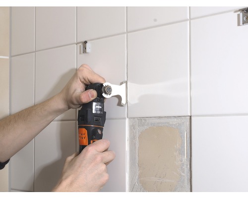 Muž odstraňuje dlaždici ze zdi multifunkčním nástrojem