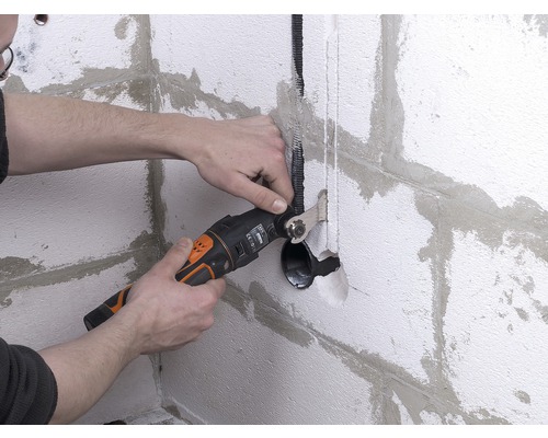 Osoba používá multifunkční nástroj k řezání zdi pro instalaci kabelů.