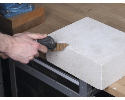 Oscilační elektrické nářadí řeže pórobetonovou tvárnici na pracovním stole.