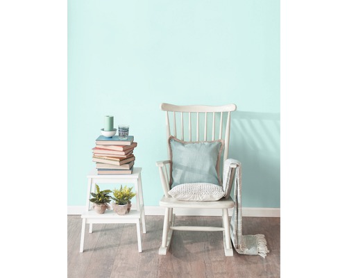 Scéna s houpacím křeslem, odkládacím stolkem, knihami a dekoracemi v světlé místnosti.