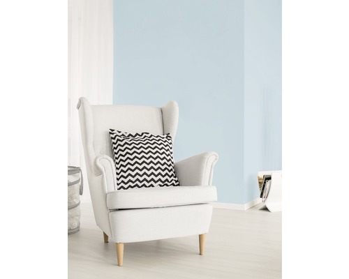 Světlý obývací pokoj s pastelově modrou barvou stěn, bílým křeslem a polštářem s cikcakovým vzorem