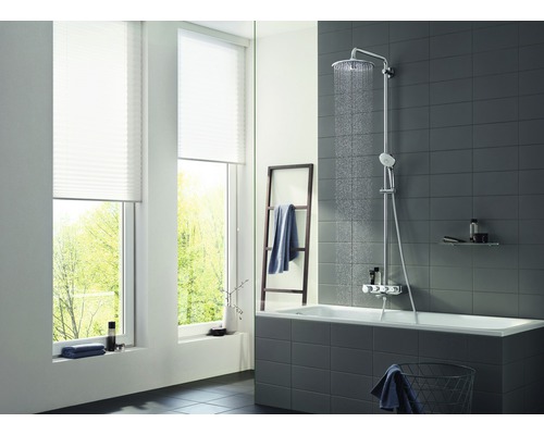 Světlá koupelna s vanou, sprchovým systémem a oknem s plisovanými žaluziemi