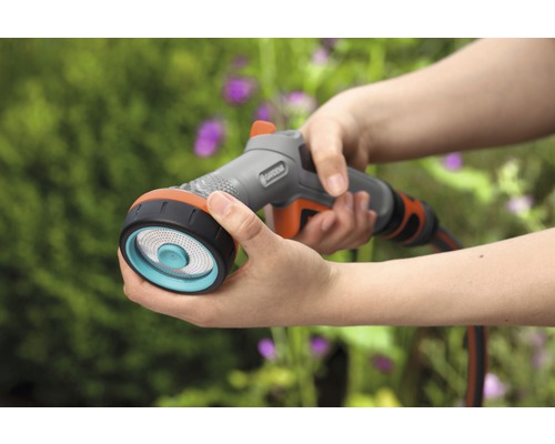 Osoba drží v ruce zavlažovací postřikovač Gardena s několika proudy.