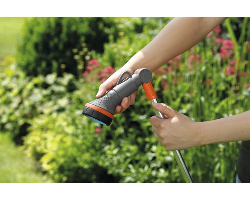 Zahradní hadice se sprchovou hlavicí v ruce před zelenými rostlinami