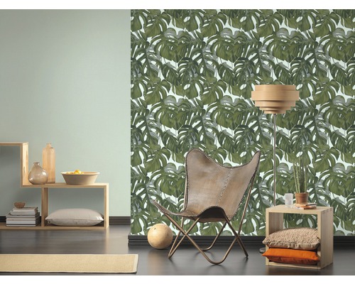 Obývací pokoj s tapetou s motivem listů Monstera, křeslem a dřevěným nábytkem pro světlé a organizované prostředí.