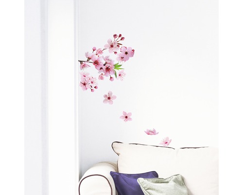 Samolepka na zeď s motivem třešňových květů na bílé zdi nad pohovkou.