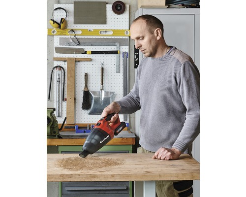 Muž vysává dřevěné piliny z ponku pomocí akumulátorového ručního vysavače Einhell.