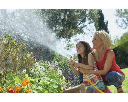 Žena a dítě zavlažují zahradní rostliny zahradní hadicí.
