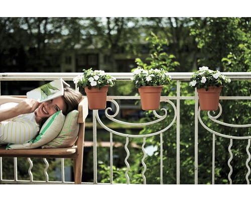 Žena relaxuje na lavičce na balkóně s truhlíky na zábradlí