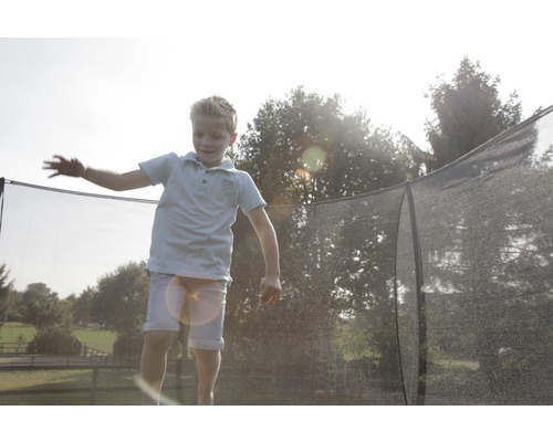 Dítě skáče na zahradní trampolíně s bezpečnostní sítí.