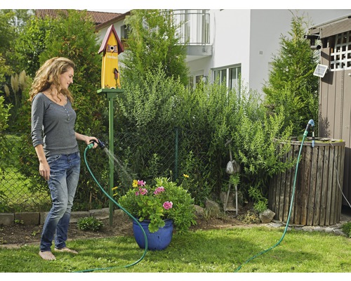 Žena zalévá květiny zahradní hadicí na zahradě.